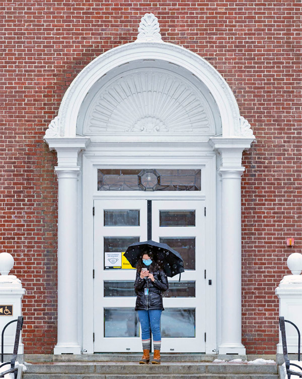 Bowdoin student in a mask with an umbrella